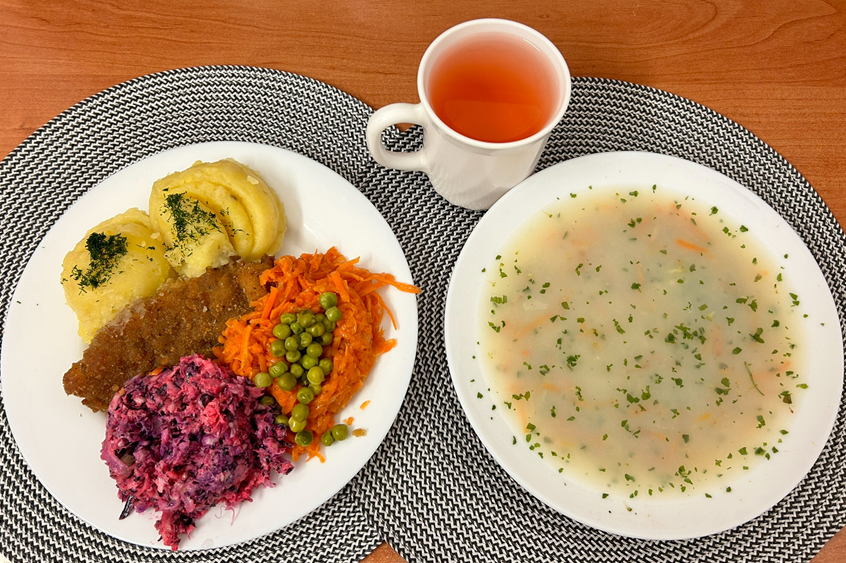 Na zdjęciu znajduje się Jarzynowa z zacierką, Ziemniaki, Kotlet drobiowy panierowany, Sos pietruszkowy, Marchewka z groszkiem oprószana, Kompot owocowy, Surówka wykwintna z olejem